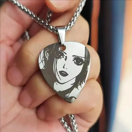Metallic guitar pick-shaped pendant with a face design held in a hand.