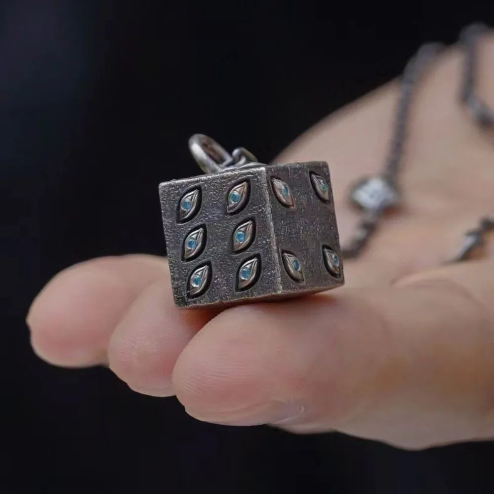 Silver square pendant with gemstones held between fingers against a dark background