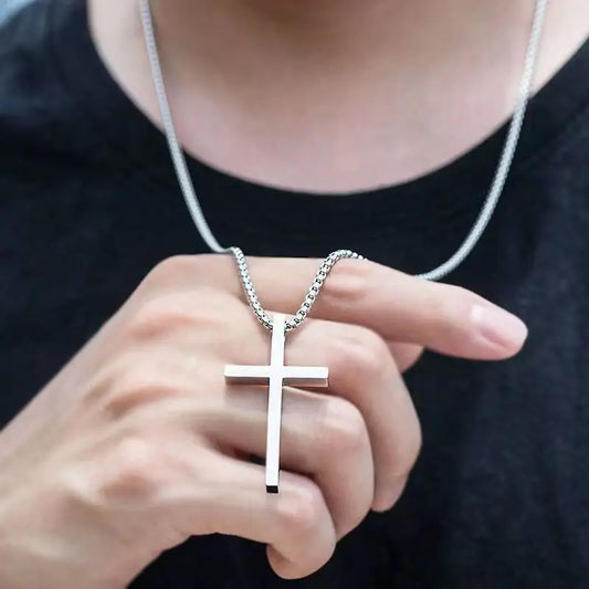 Person holding a silver cross necklace against a dark background