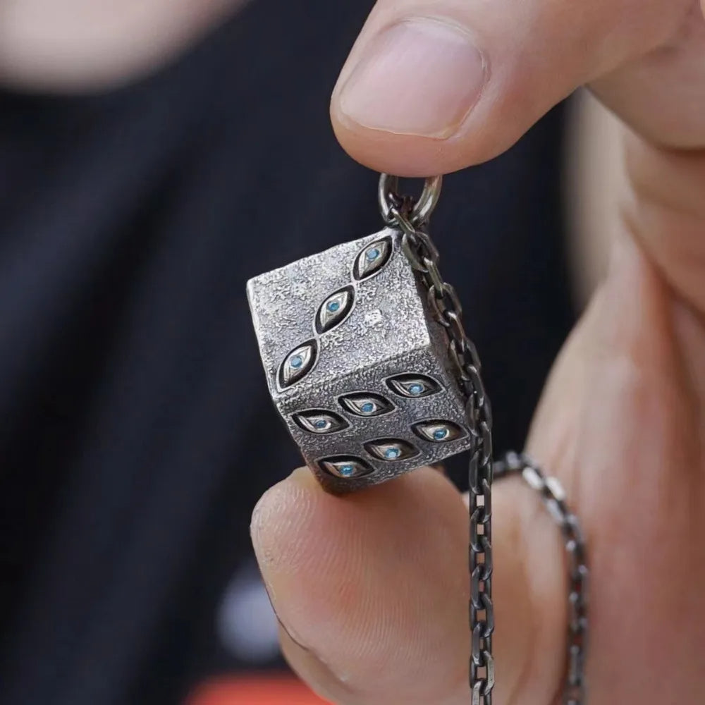 Close-up of a hand holding a silver pendant with intricate designs.