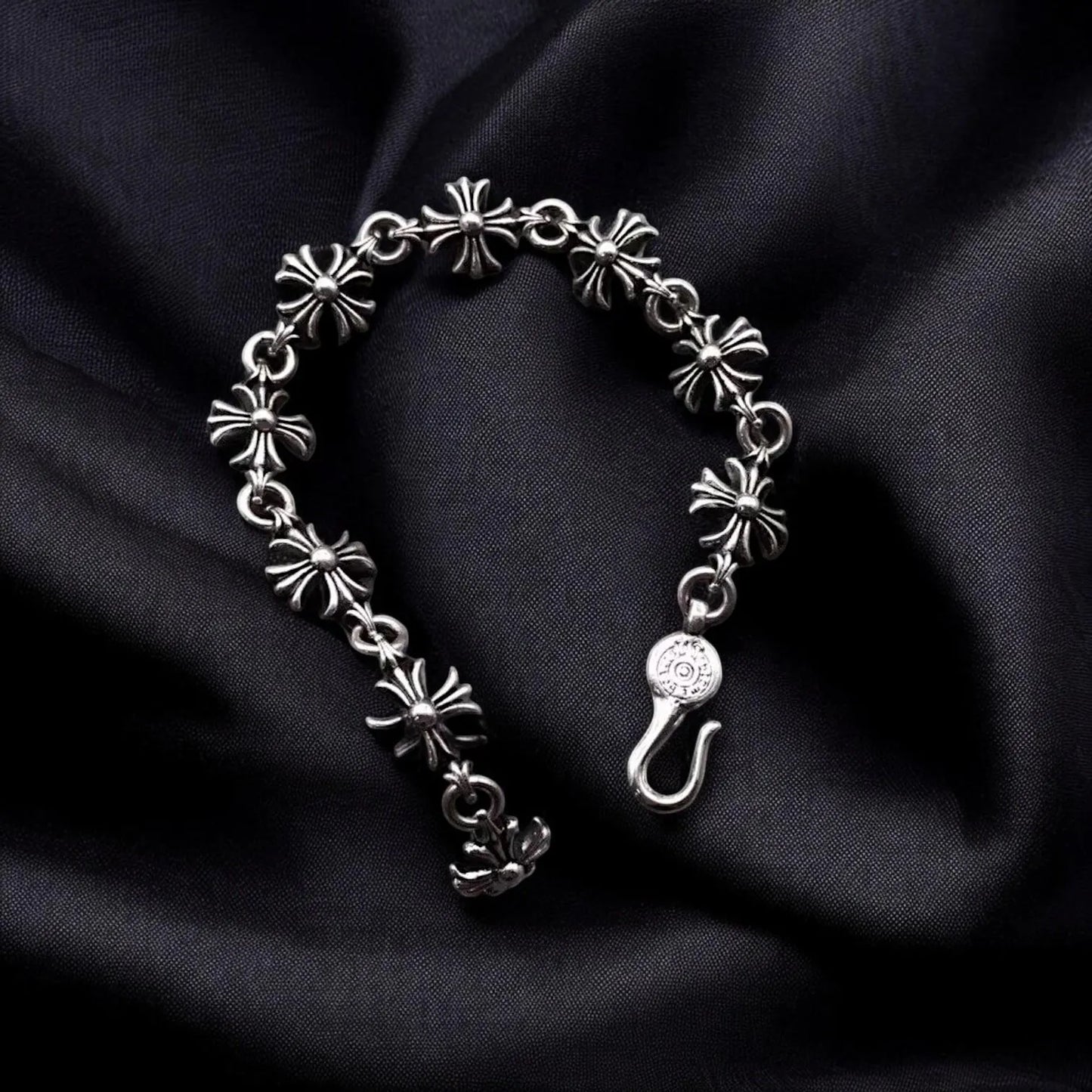 Silver bracelet with floral designs on black satin background