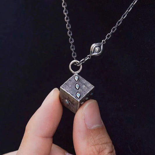 Silver cube pendant necklace held by a hand against a dark background