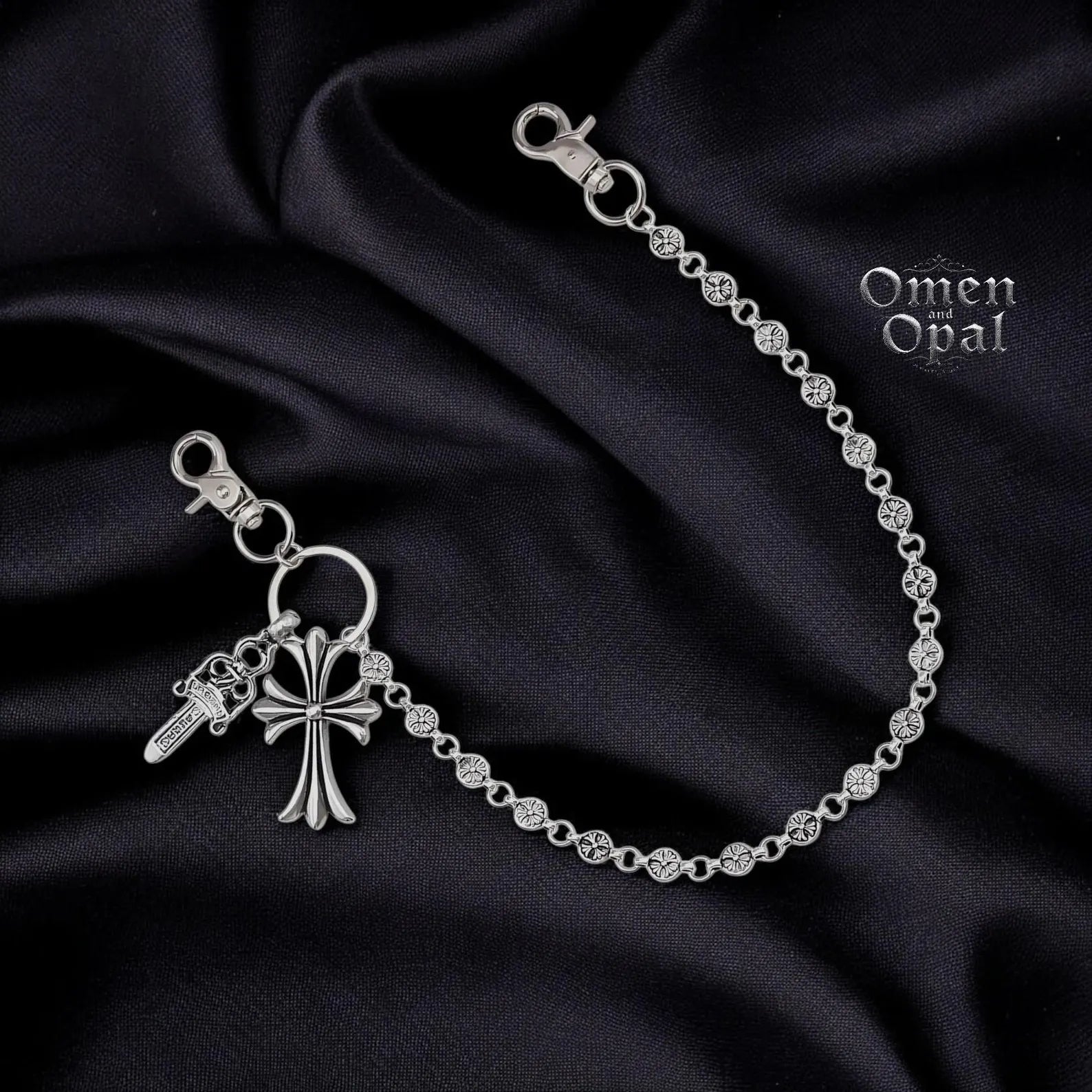 Silver bracelet with key and cross charm on a dark fabric background