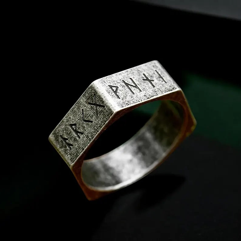 Silver ring with engraved symbols on a dark background