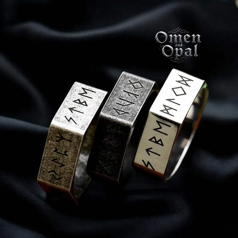 Three Gothic Hexagon Viking Rings made of stainless steel, displayed on a dark fabric background. The rings feature runic inscriptions and a hexagonal shape.