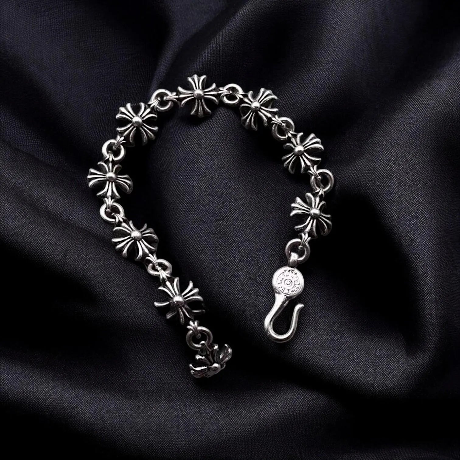 Silver bracelet with floral designs on black satin background